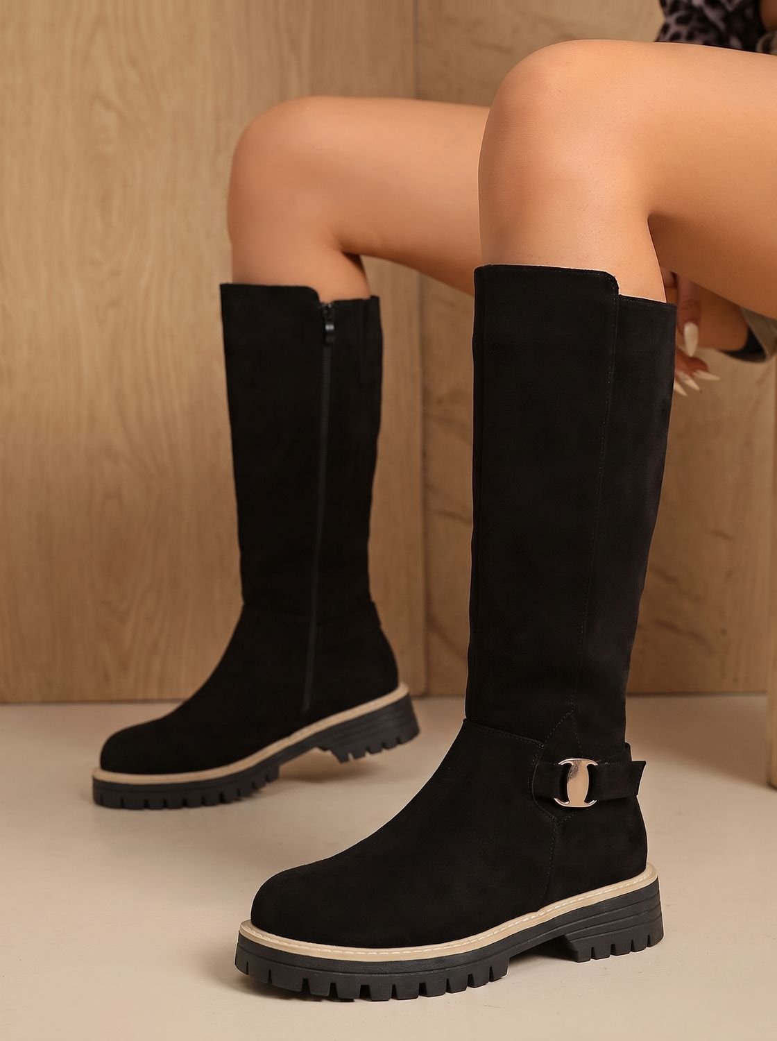 Pair of black knee-high boots displayed from the side, with visible side zippers, ankle buckles, and raised treaded soles.