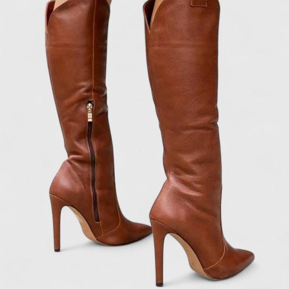 Brown knee-high pointed-toe boots shown in side view, highlighting the outer side zip and tall stiletto heels.