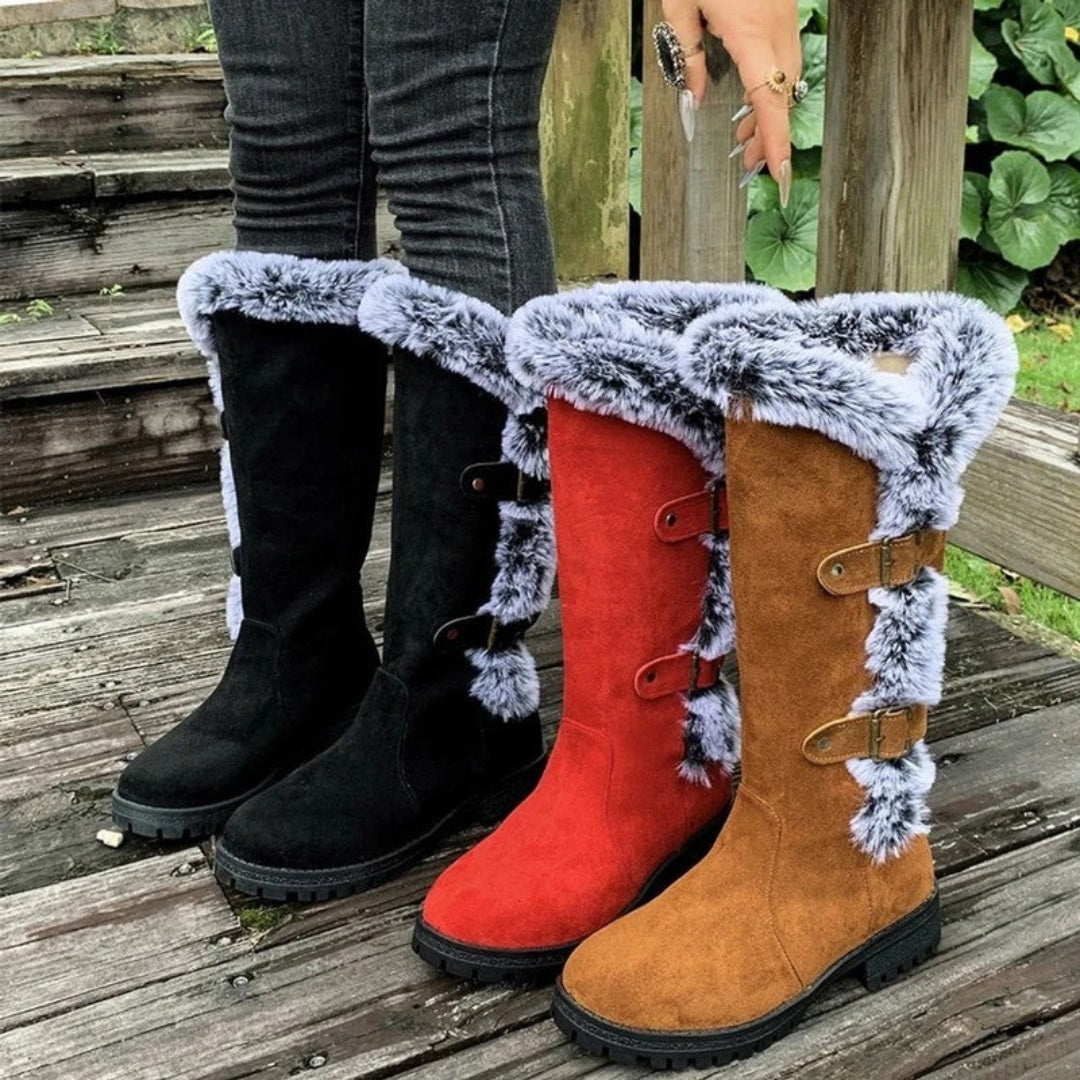 Black, red, and tan knee-high winter boots lined up together, displaying their contrasting faux fur cuffs, side buckles, and low rugged heels.