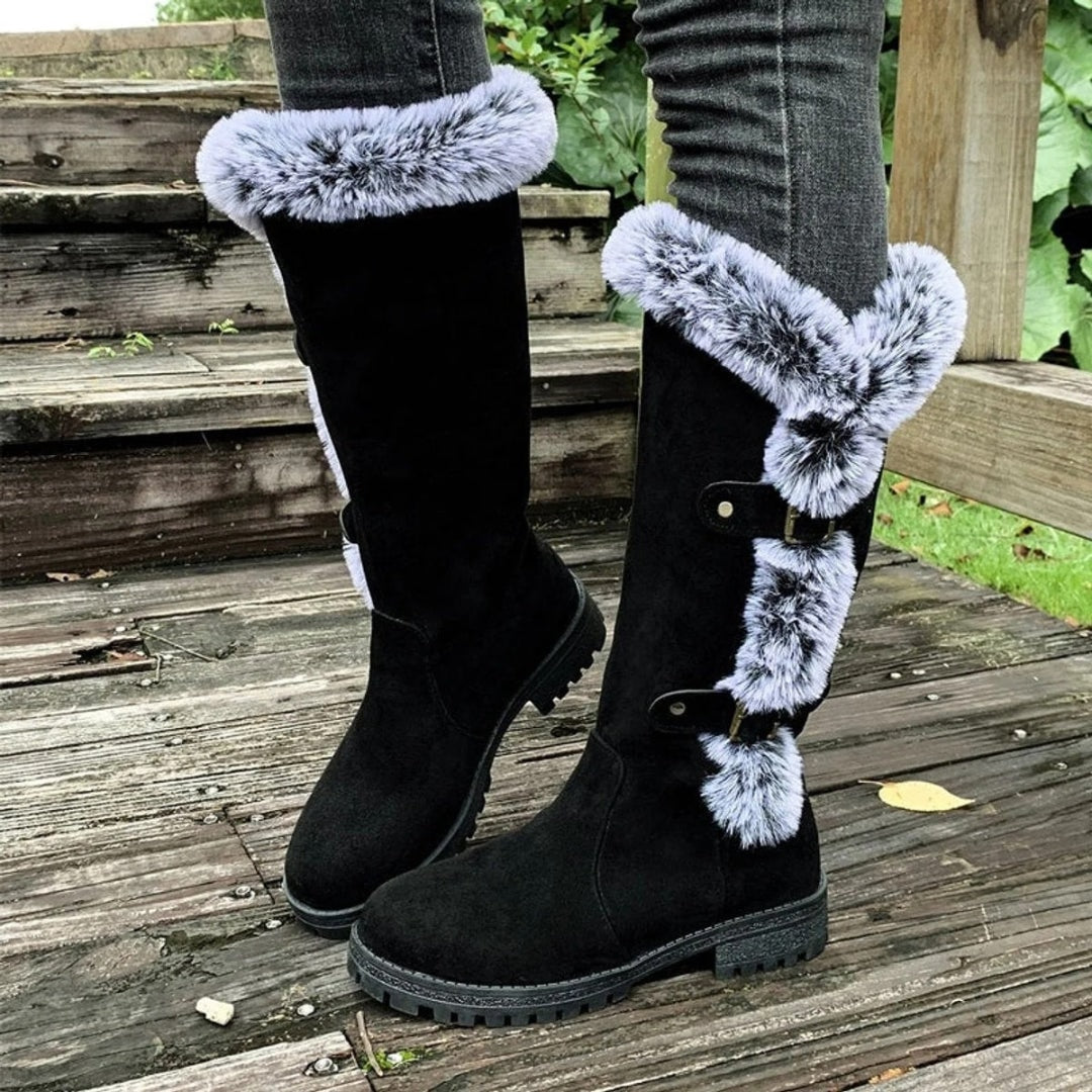 Black tall winter boots displayed together, highlighting the plush faux fur upper trim and layered buckle details on one outer side.
