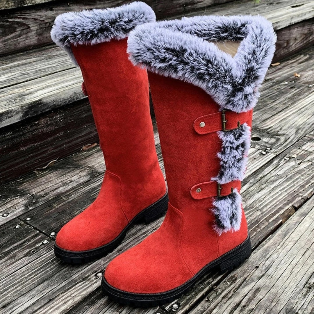 Close view of red knee-high boots featuring oversized faux fur cuffs, decorative side buckles, rounded toes, and sturdy lug soles.