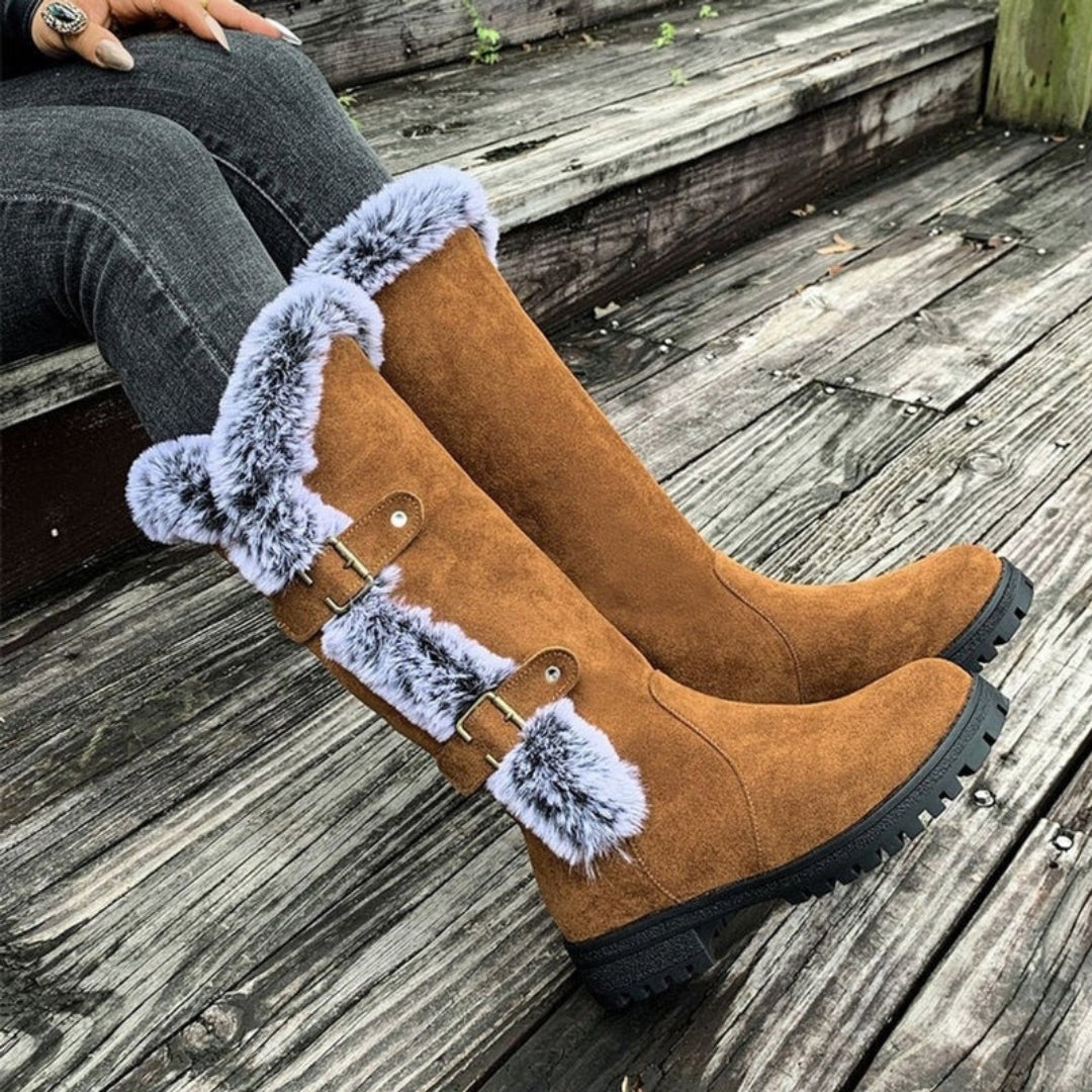 Tan winter boots resting on a deck, emphasizing the plush faux fur cuffs and two side buckle straps along the tall shafts.