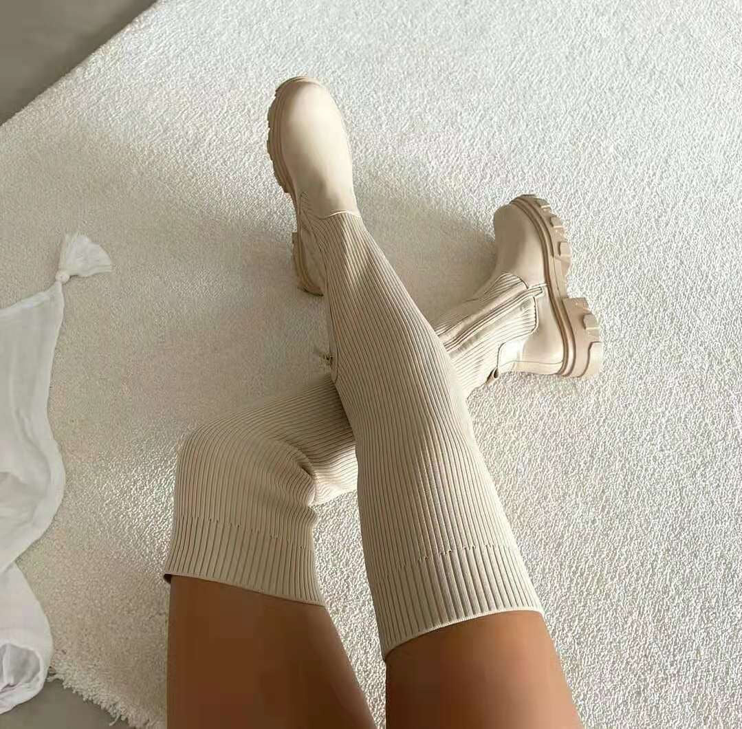 Cream knee-high boots arranged on a light surface, with ribbed shafts, visible side zippers, and chunky lug soles.