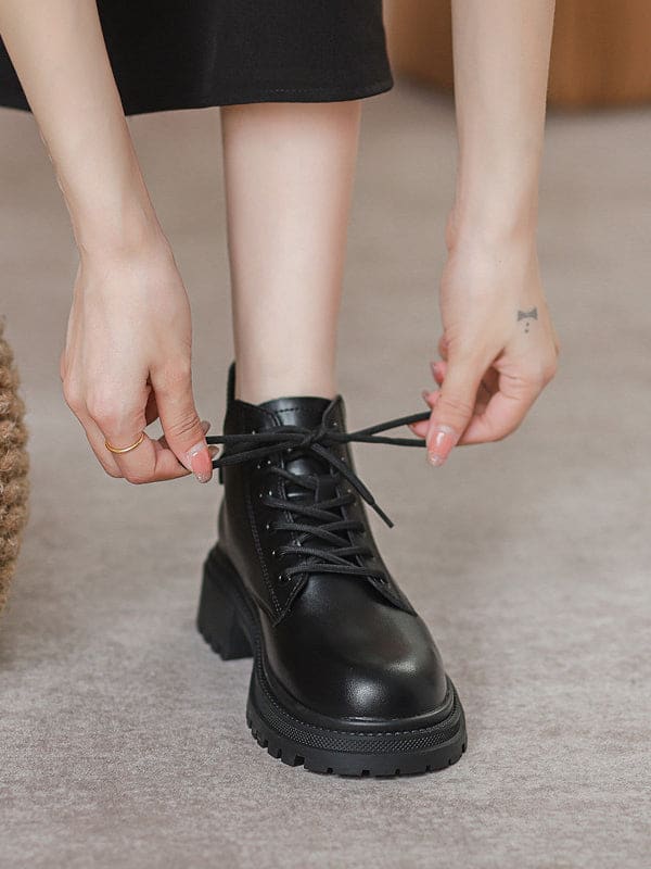 Person lacing up black combat boots with round toe and platform sole while wearing a black skirt._0