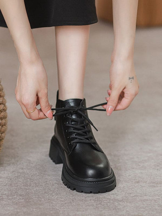 Person lacing up black combat boots with round toe and platform sole while wearing a black skirt._0