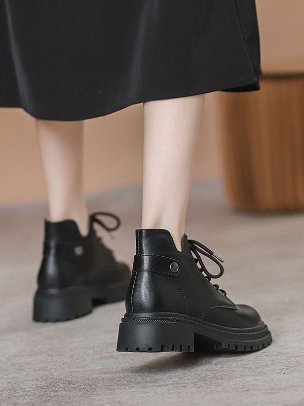 Person lacing up black combat boots with round toe and platform sole while wearing a black skirt._5