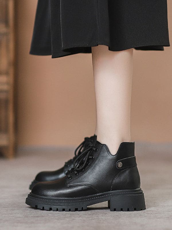 Person lacing up black combat boots with round toe and platform sole while wearing a black skirt._9
