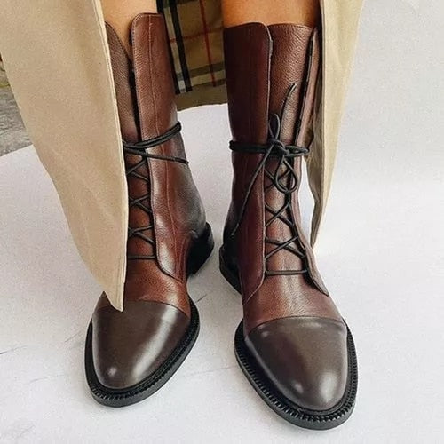 Brown mid-calf lace-up boots with dark glossy cap toes styled beneath a long beige coat.