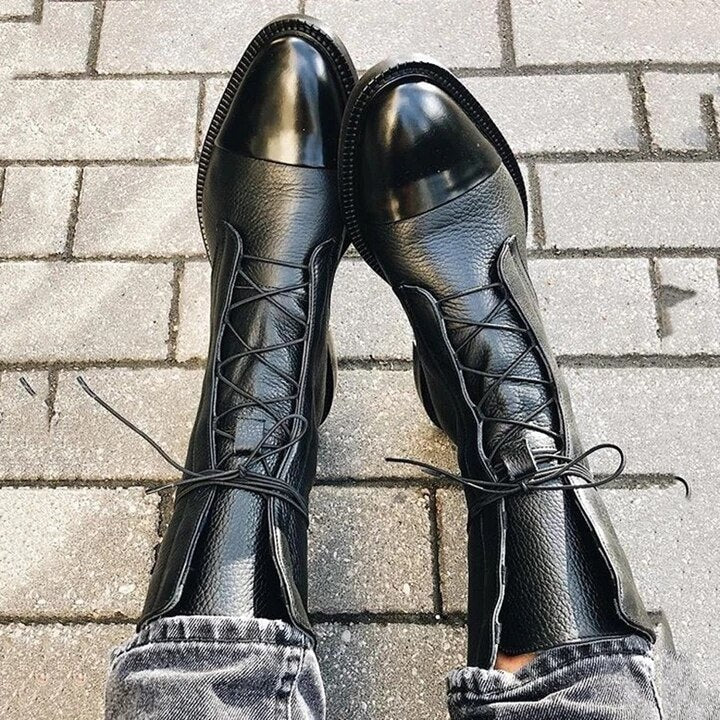 Black lace-up boots arranged on gray paving, highlighting their rounded cap toes and long laces.
