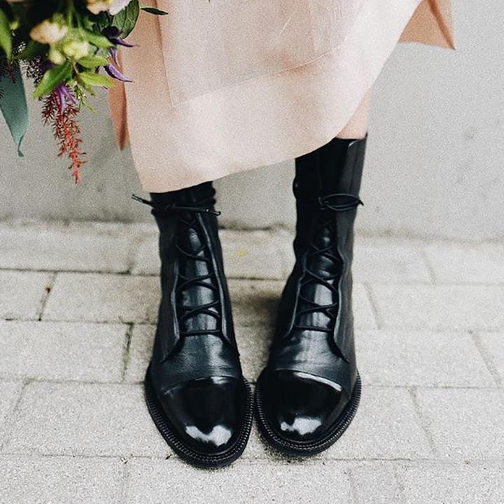 Black lace-up boots paired with a flowing light skirt, showing their tall silhouette and polished toes.