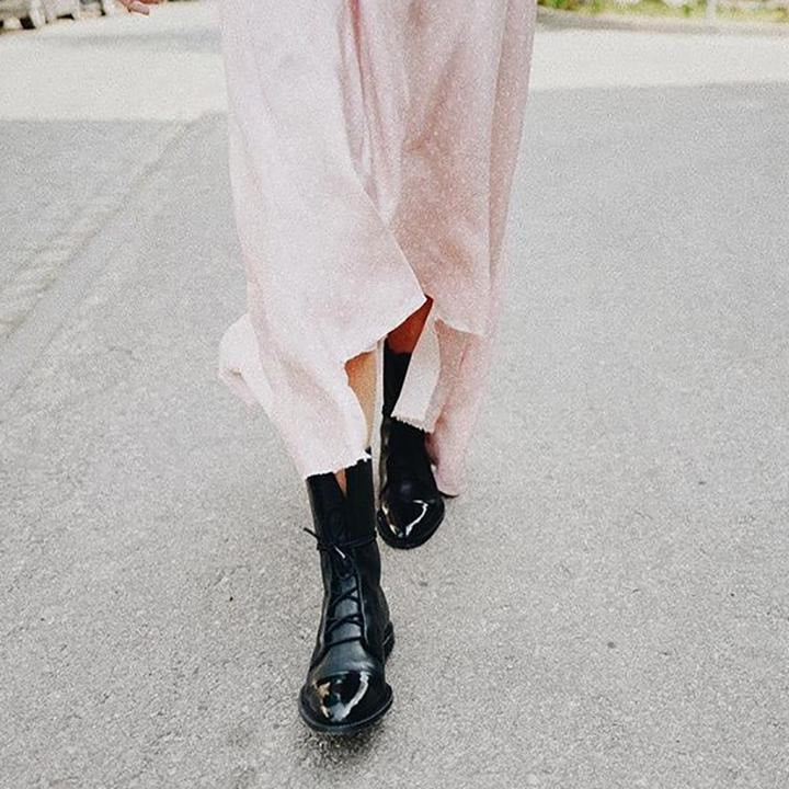 A walking view of black mid-calf lace-up boots beneath a light flowing outfit.
