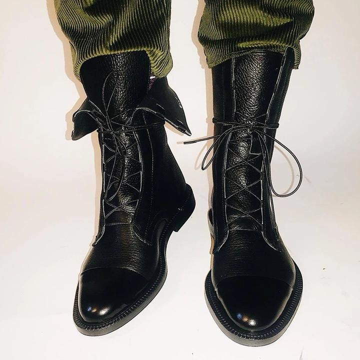 Black mid-calf lace-up boots worn with green trousers, showing tied laces, side panels, and low heels.