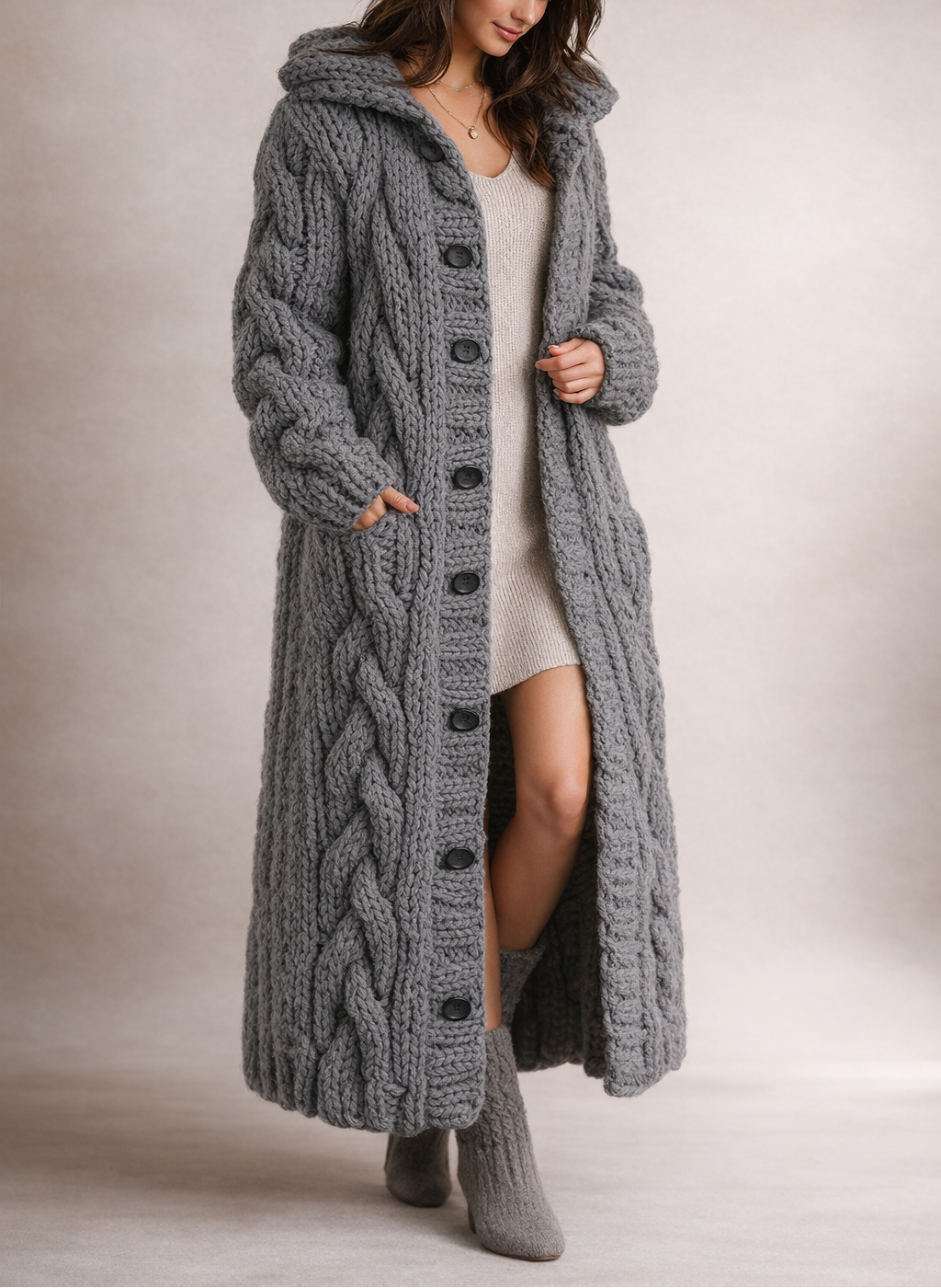 Full-length view of a charcoal long cable-knit cardigan coat with a hood, button front, and side pockets, styled over a light outfit.