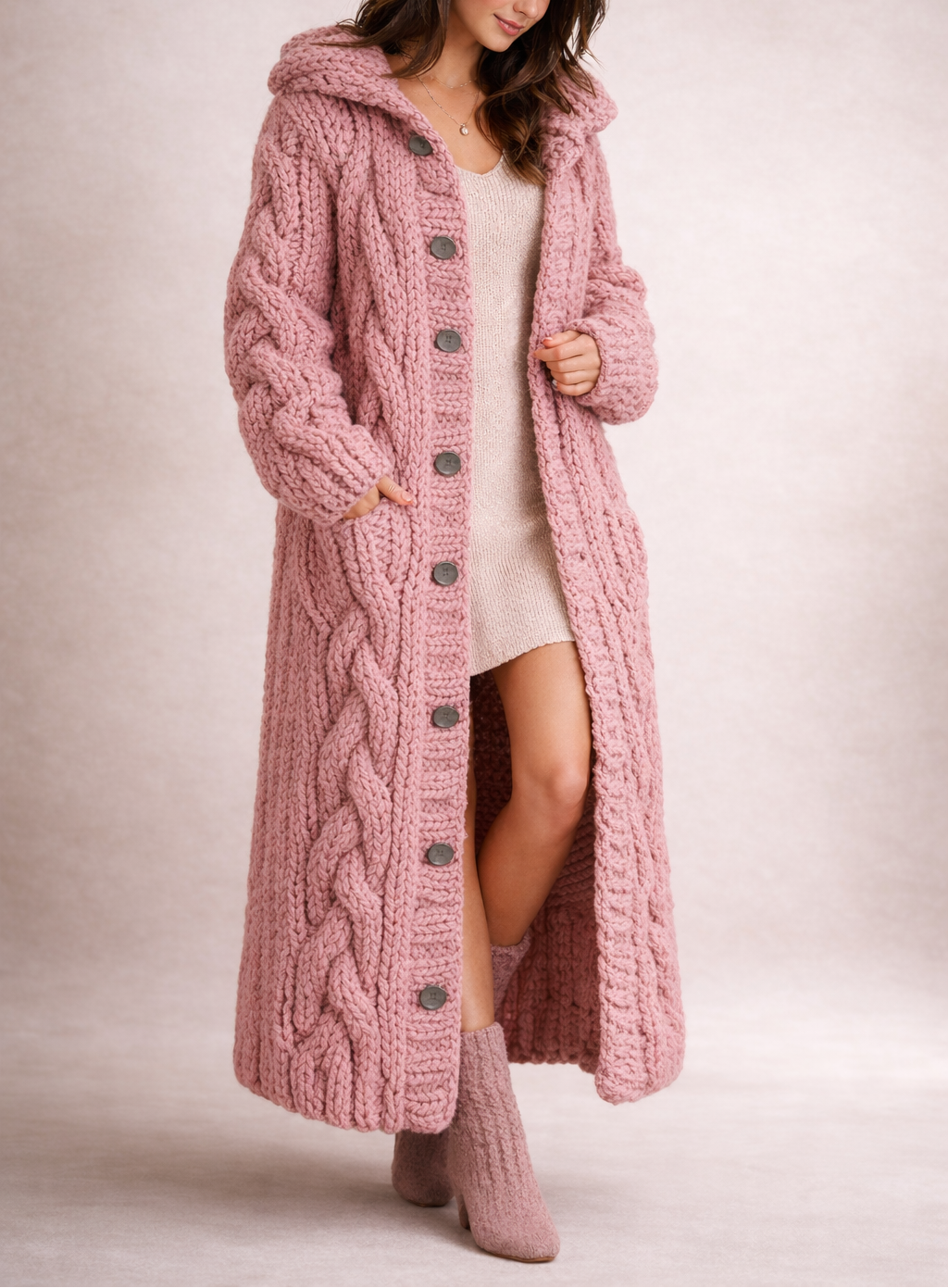 Full-length view of the pink hooded cable-knit cardigan coat with chunky braided texture, dark buttons, and a long open hem.