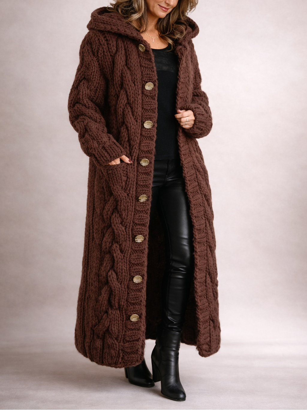 Dark brown long hooded cardigan coat featuring prominent cable-knit panels, contrasting buttons, and a sweeping full-length silhouette.