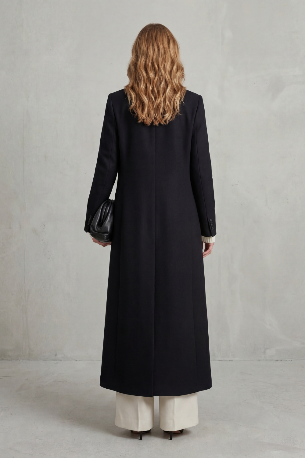 Back view of the black long tailored coat, showing its clean uninterrupted length, long sleeves and back shaping.