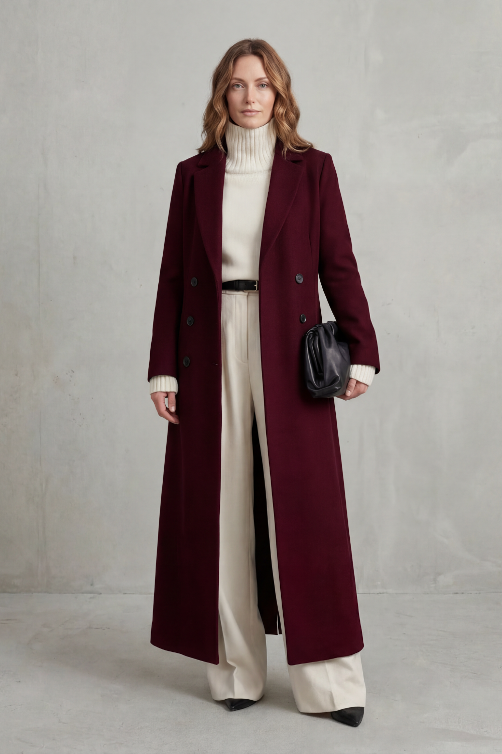 Deep burgundy double-breasted coat shown fully from the front, with its long structured shape layered over a cream turtleneck and trousers.