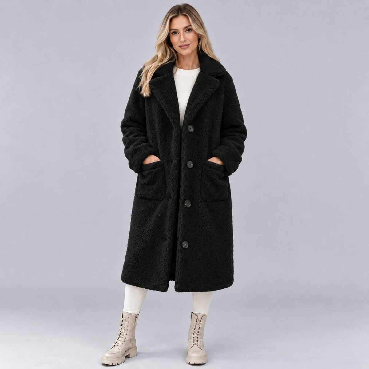 Model wearing a long black faux fur coat with a wide lapel collar, button front, long sleeves, and two patch pockets.