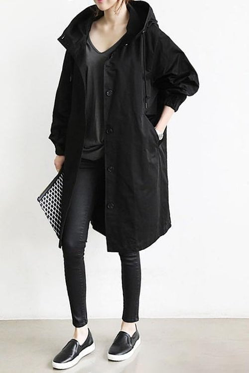 Black long hooded coat styled with black leggings and slip-on shoes, showing its buttoned front, roomy hood, and side pockets.