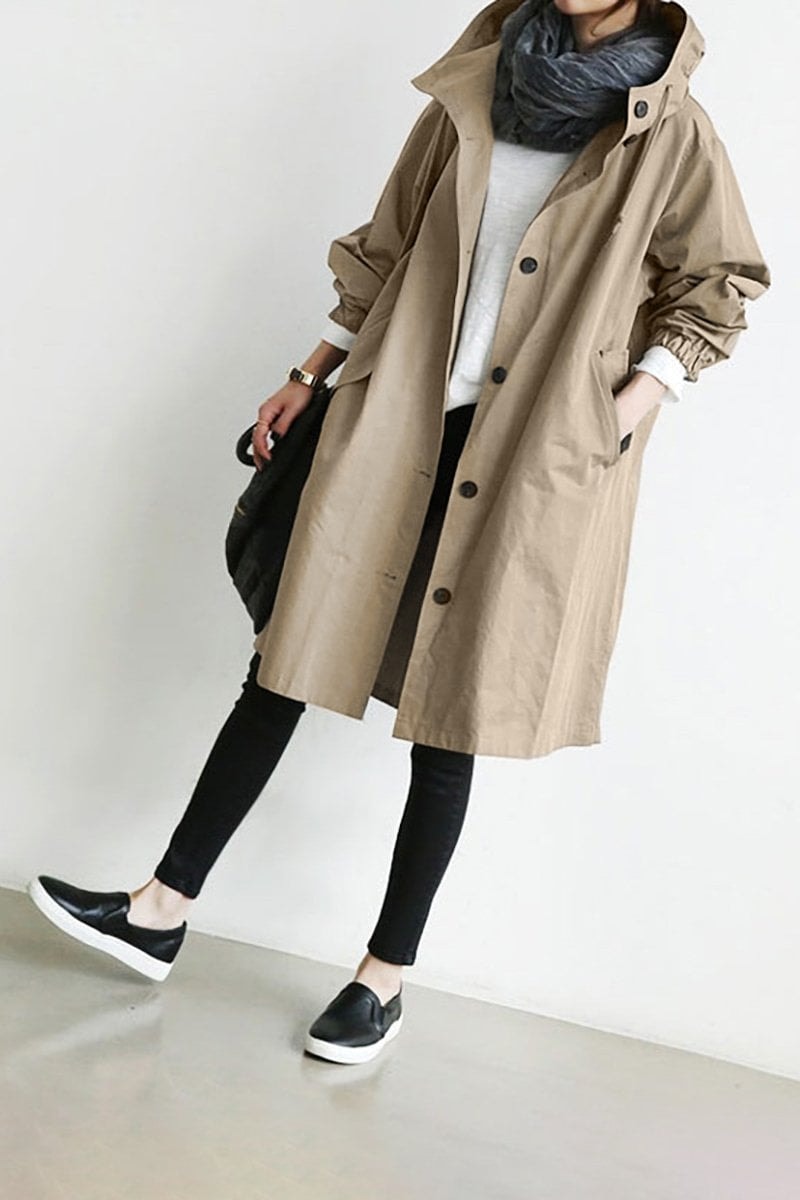 Tan long hooded coat worn with the front partly open, displaying its button closure, high hood, side pockets, and gathered cuffs.