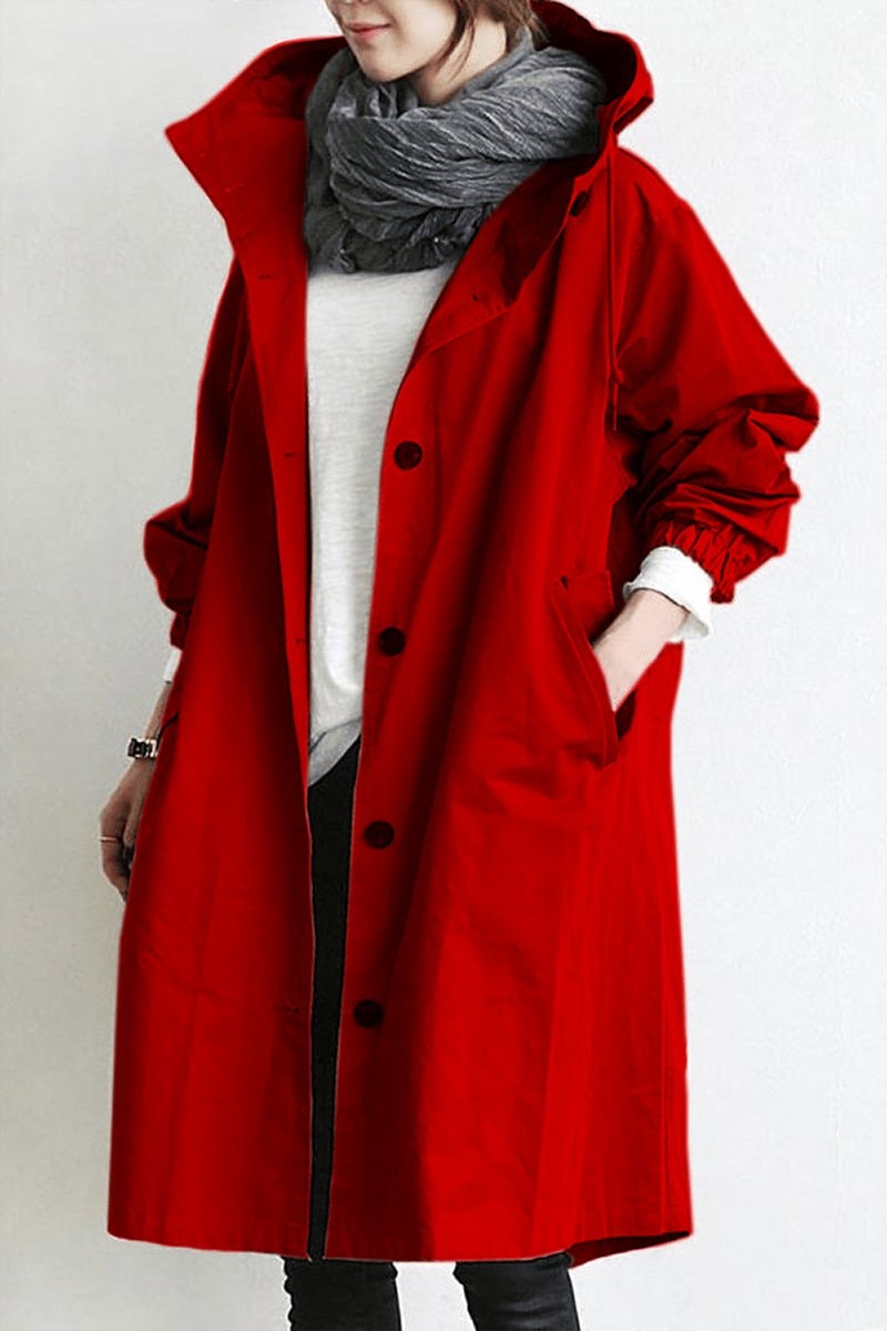 Bright red long hooded coat viewed from the front, featuring a row of dark buttons, raised hood, and hands placed in the side pockets.