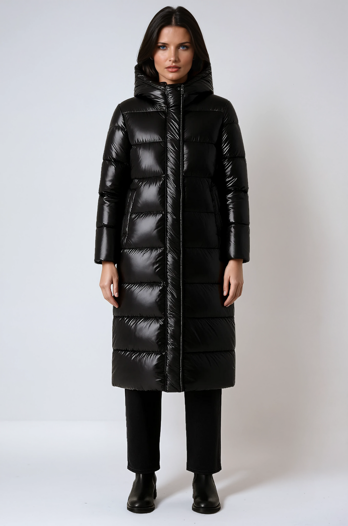 Front view of a long black hooded quilted jacket styled with black trousers and boots.