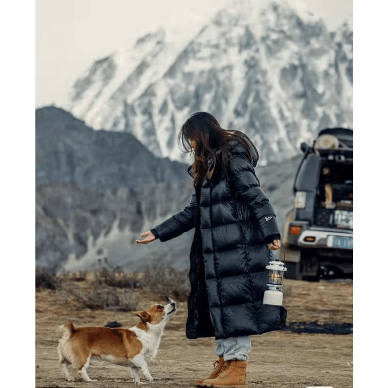 Side view of the long black hooded quilted jacket worn outdoors beside a dog and vehicle.