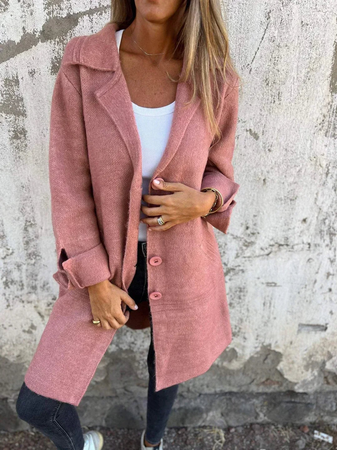 Pink button-front blazer jacket styled with one hand at the fastening, highlighting the long tailored shape and cuff details.