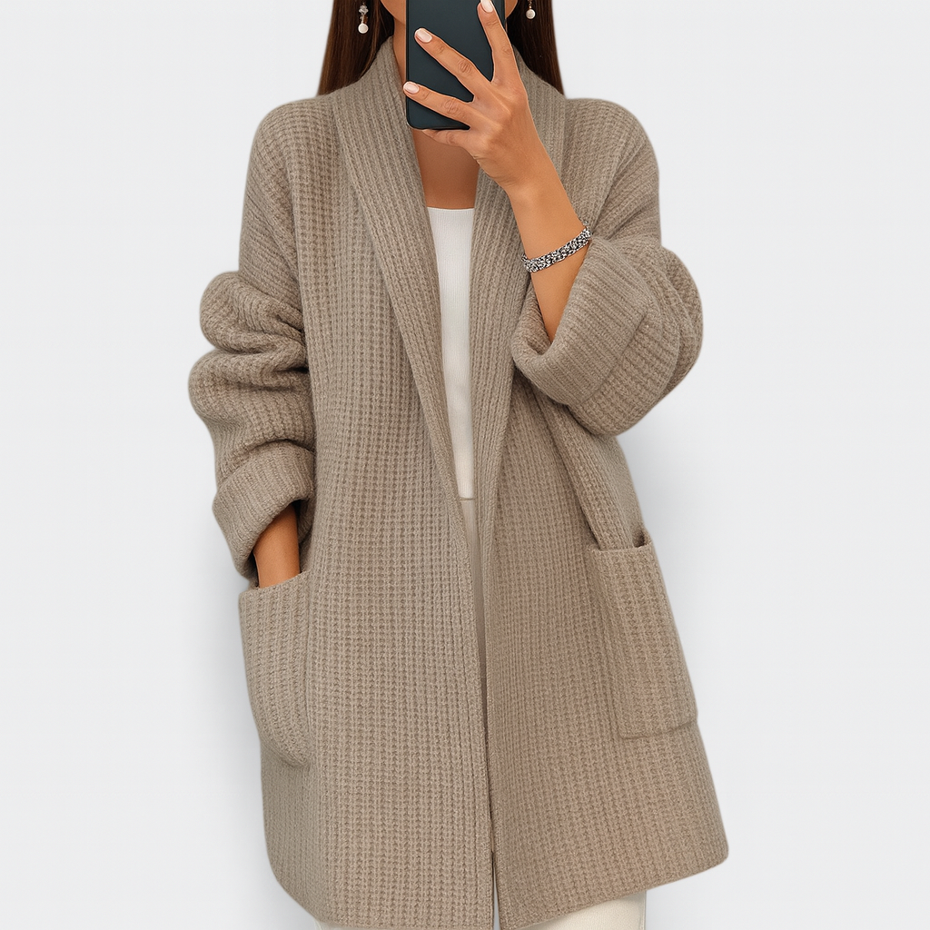 Taupe longline open-front cardigan with long sleeves, ribbed cuffs, and roomy patch pockets, shown layered over a light top.