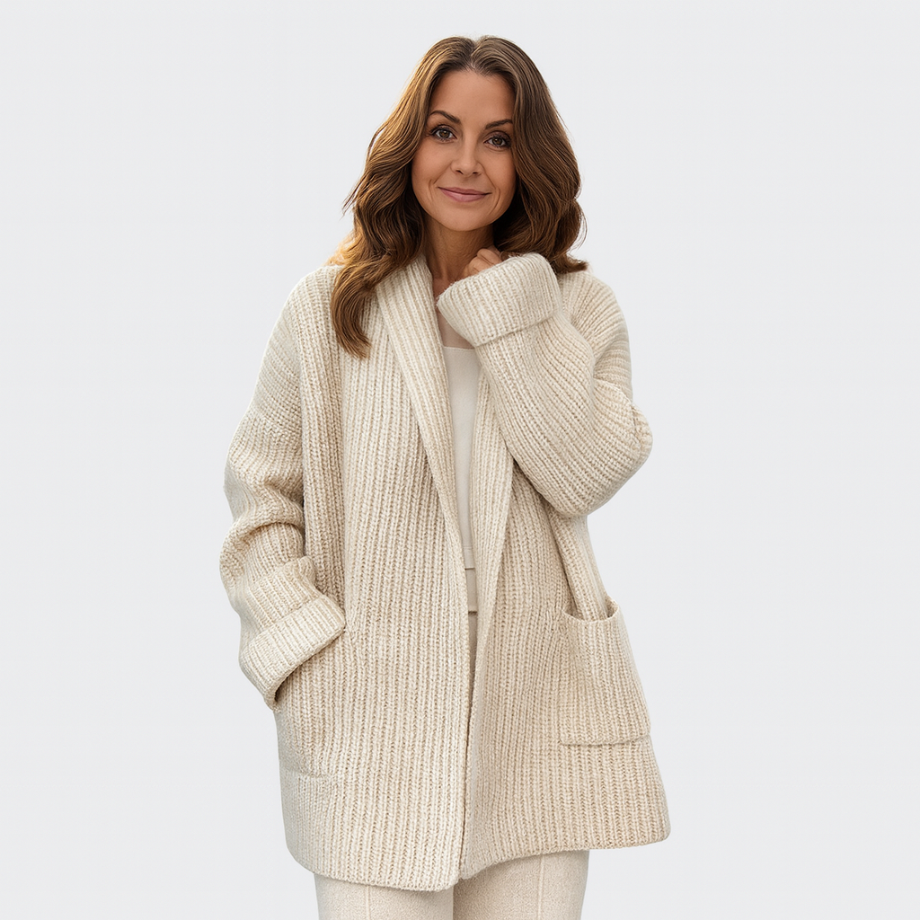 Cream longline open-front cardigan modeled with one hand in a patch pocket, highlighting its relaxed fit and ribbed cuffs.