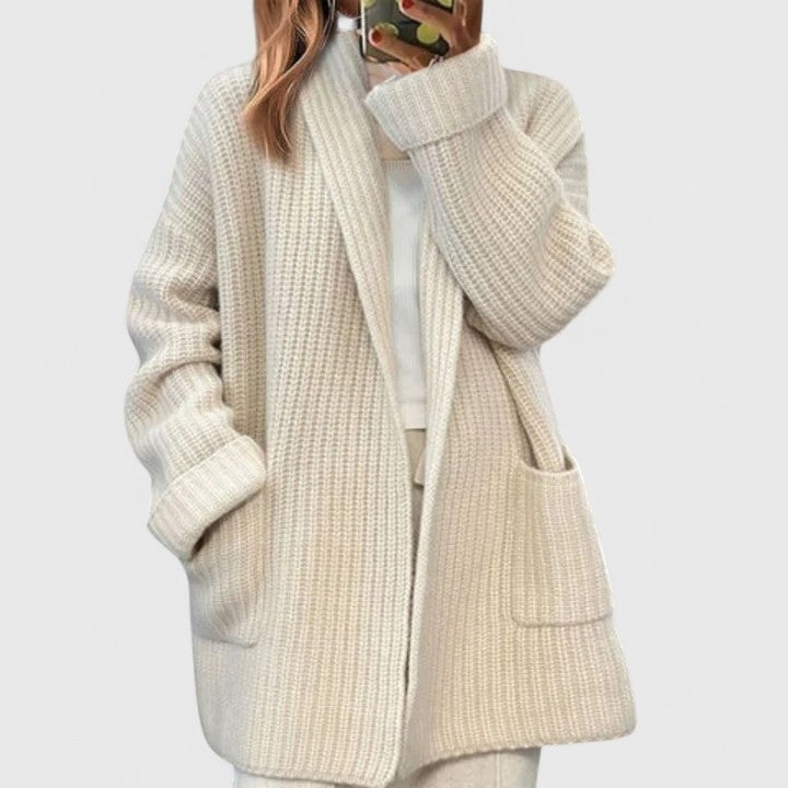 Light beige open-front cardigan shown at a slight angle, with its longline hem, textured knit appearance, and front patch pockets visible.