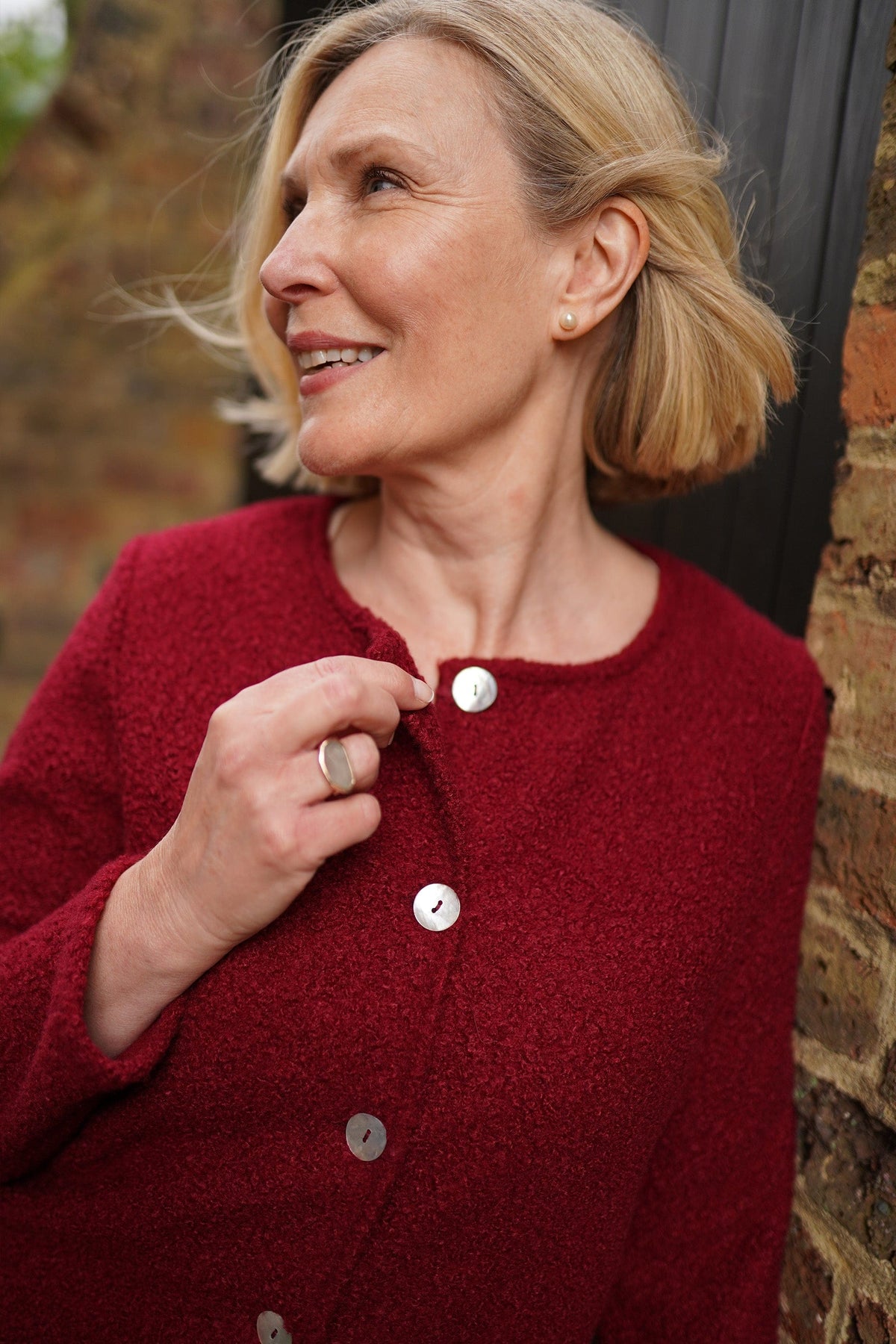 Woman wearing a textured bouclé collarless cardigan jacket with round wooden buttons down the front and long sleeves, over a light top and dark trousers._3