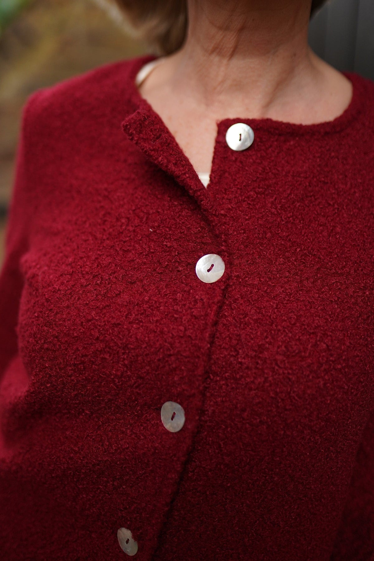 Woman wearing a textured bouclé collarless cardigan jacket with round wooden buttons down the front and long sleeves, over a light top and dark trousers._4