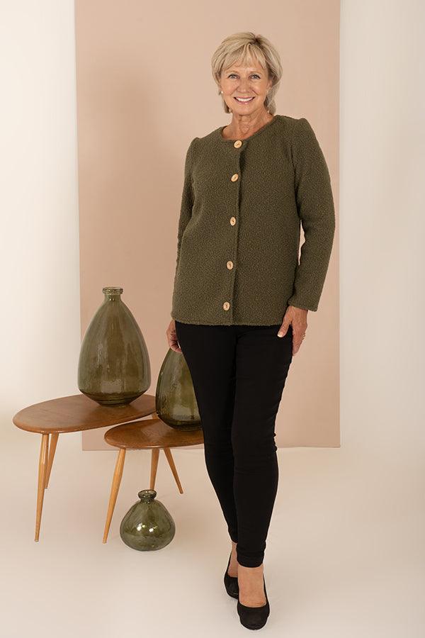 Woman wearing a textured bouclé collarless cardigan jacket with round wooden buttons down the front and long sleeves, over a light top and dark trousers._6