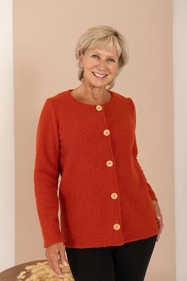 Woman wearing a textured bouclé collarless cardigan jacket with round wooden buttons down the front and long sleeves, over a light top and dark trousers._8