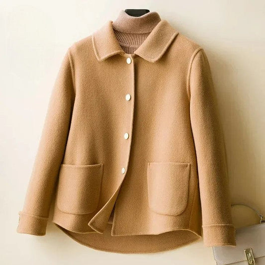 A short coat with a rounded collar, front snap buttons, and curved patch pockets displayed over a ribbed high-neck top._0