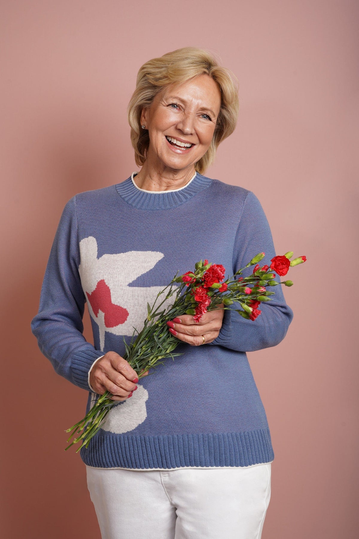 Woman wearing a long sleeve crew neck knit jumper with a large intarsia flower motif on the front, ribbed neckline, cuffs and hem, with trousers._1