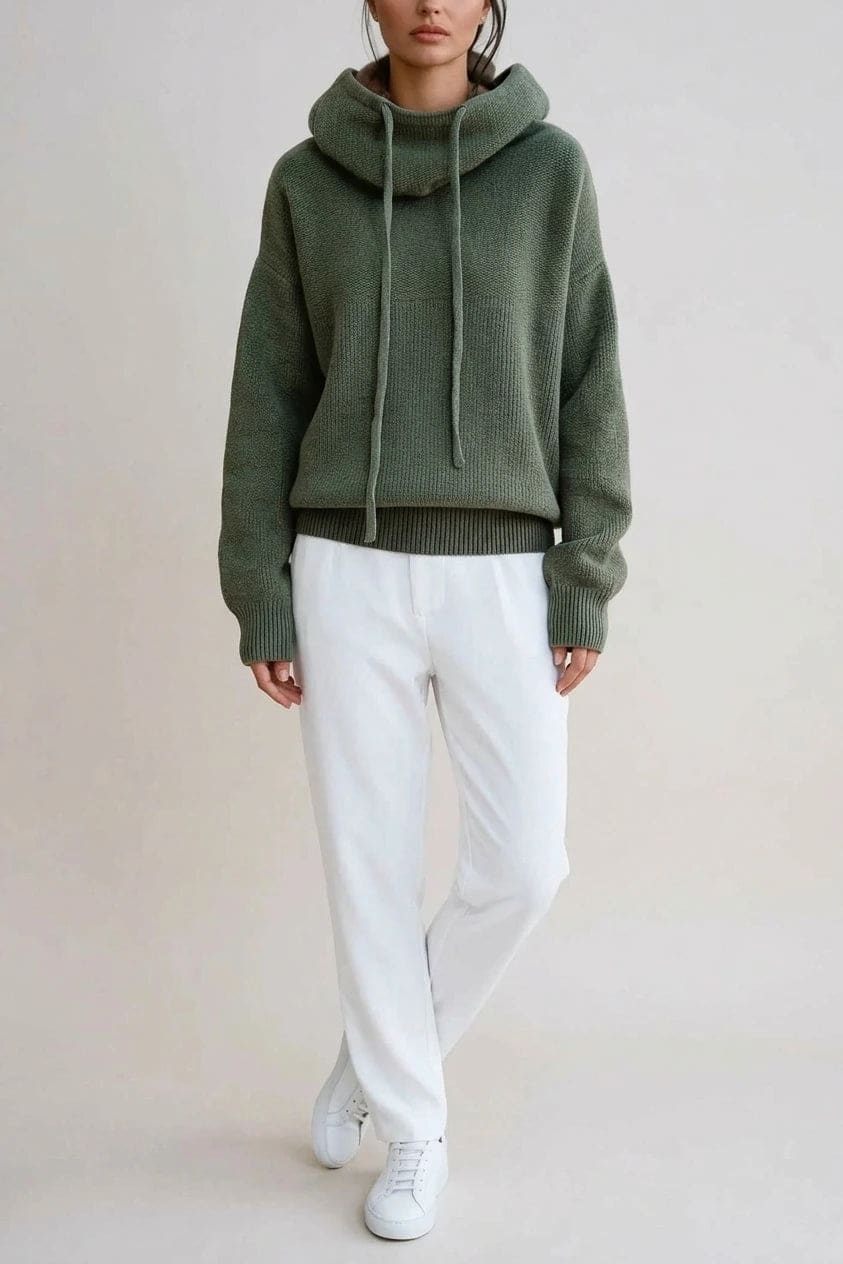 Woman wearing an oversized knitted hooded jumper with drawstring, dropped shoulders and a deep ribbed hem, with straight trousers and trainers._0