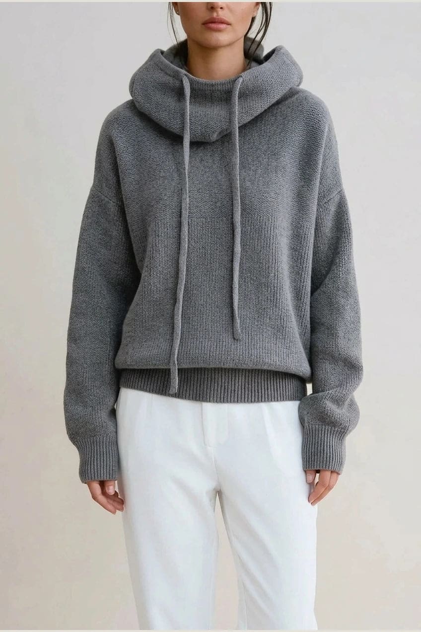 Woman wearing an oversized knitted hooded jumper with drawstring, dropped shoulders and a deep ribbed hem, with straight trousers and trainers._1