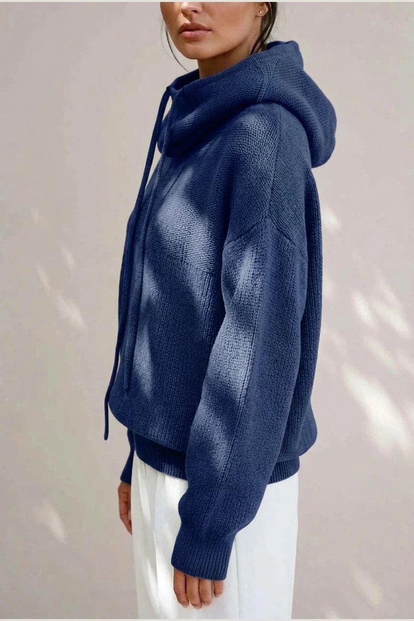 Woman wearing an oversized knitted hooded jumper with drawstring, dropped shoulders and a deep ribbed hem, with straight trousers and trainers._10