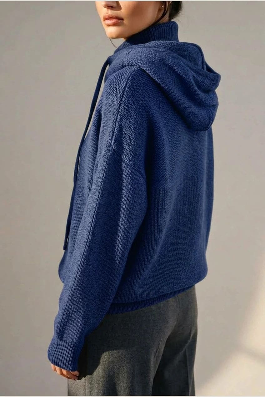 Woman wearing an oversized knitted hooded jumper with drawstring, dropped shoulders and a deep ribbed hem, with straight trousers and trainers._11
