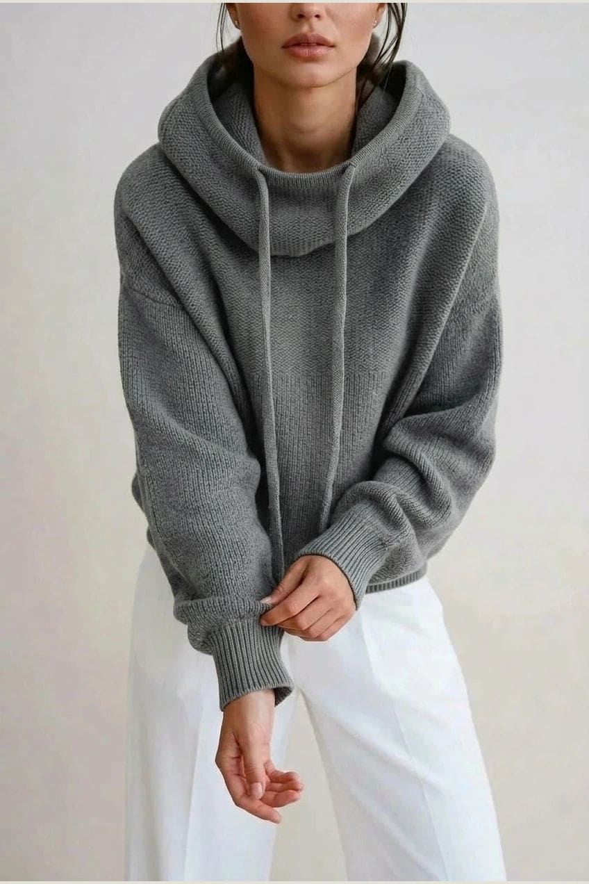 Woman wearing an oversized knitted hooded jumper with drawstring, dropped shoulders and a deep ribbed hem, with straight trousers and trainers._2
