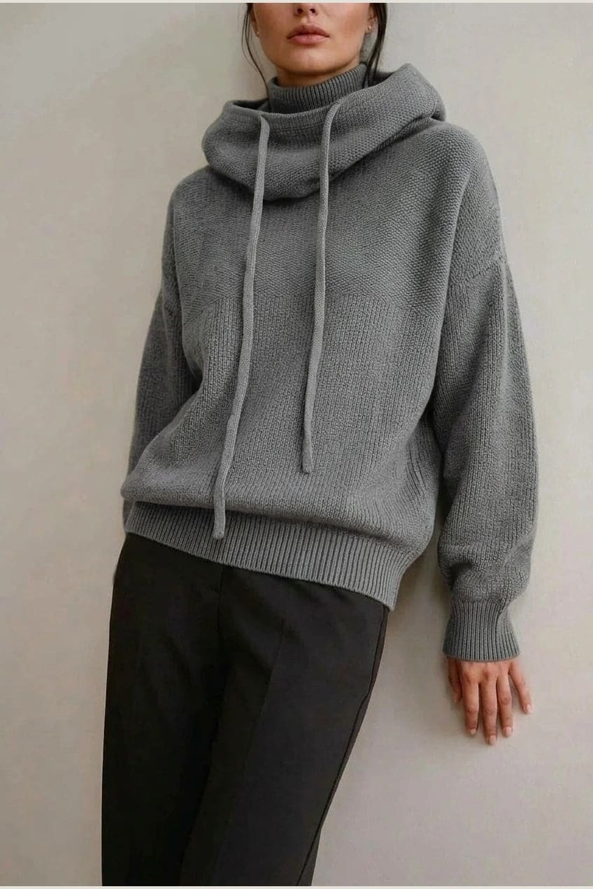 Woman wearing an oversized knitted hooded jumper with drawstring, dropped shoulders and a deep ribbed hem, with straight trousers and trainers._3