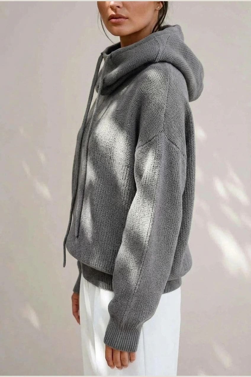 Woman wearing an oversized knitted hooded jumper with drawstring, dropped shoulders and a deep ribbed hem, with straight trousers and trainers._4