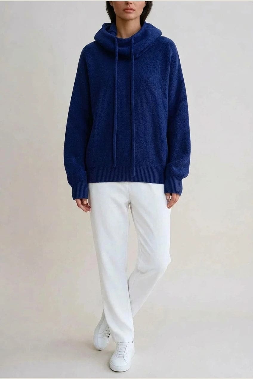 Woman wearing an oversized knitted hooded jumper with drawstring, dropped shoulders and a deep ribbed hem, with straight trousers and trainers._7