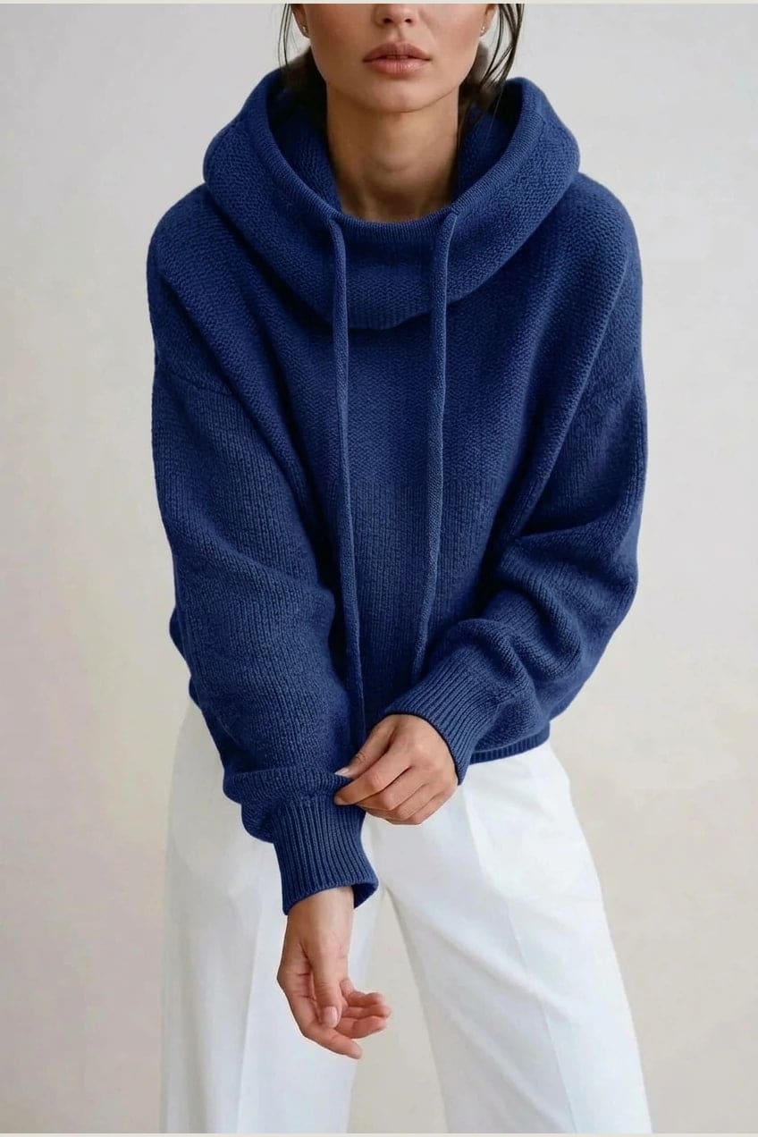 Woman wearing an oversized knitted hooded jumper with drawstring, dropped shoulders and a deep ribbed hem, with straight trousers and trainers._8
