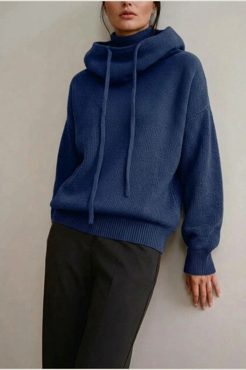 Woman wearing an oversized knitted hooded jumper with drawstring, dropped shoulders and a deep ribbed hem, with straight trousers and trainers._9