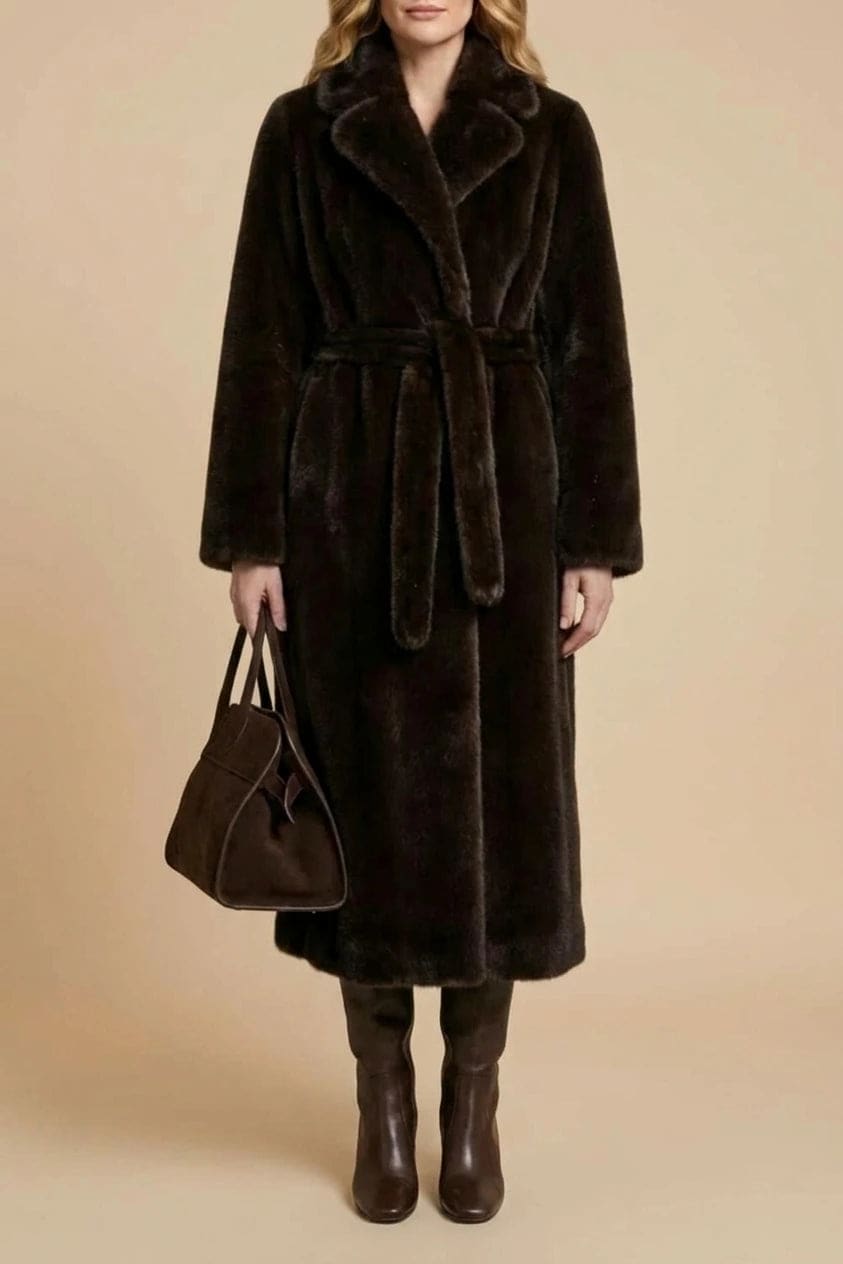 Woman wearing a long belted faux fur coat with notch lapels, tie waist and full-length sleeves, holding a suede tote and wearing knee-high boots._0