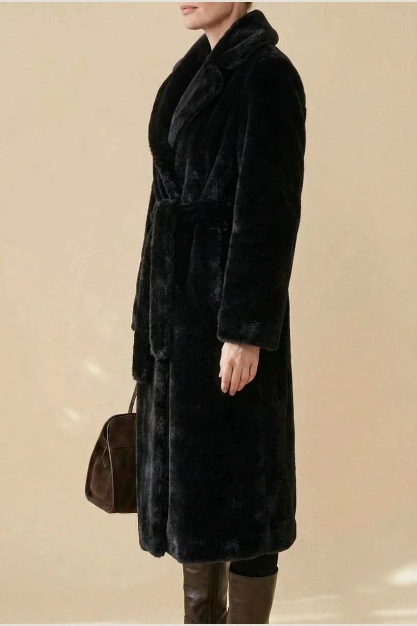 Woman wearing a long belted faux fur coat with notch lapels, tie waist and full-length sleeves, holding a suede tote and wearing knee-high boots._10