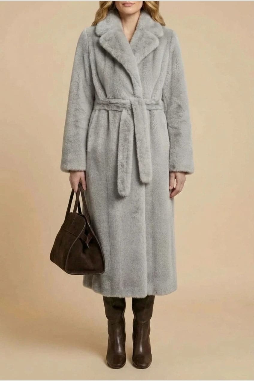 Woman wearing a long belted faux fur coat with notch lapels, tie waist and full-length sleeves, holding a suede tote and wearing knee-high boots._13